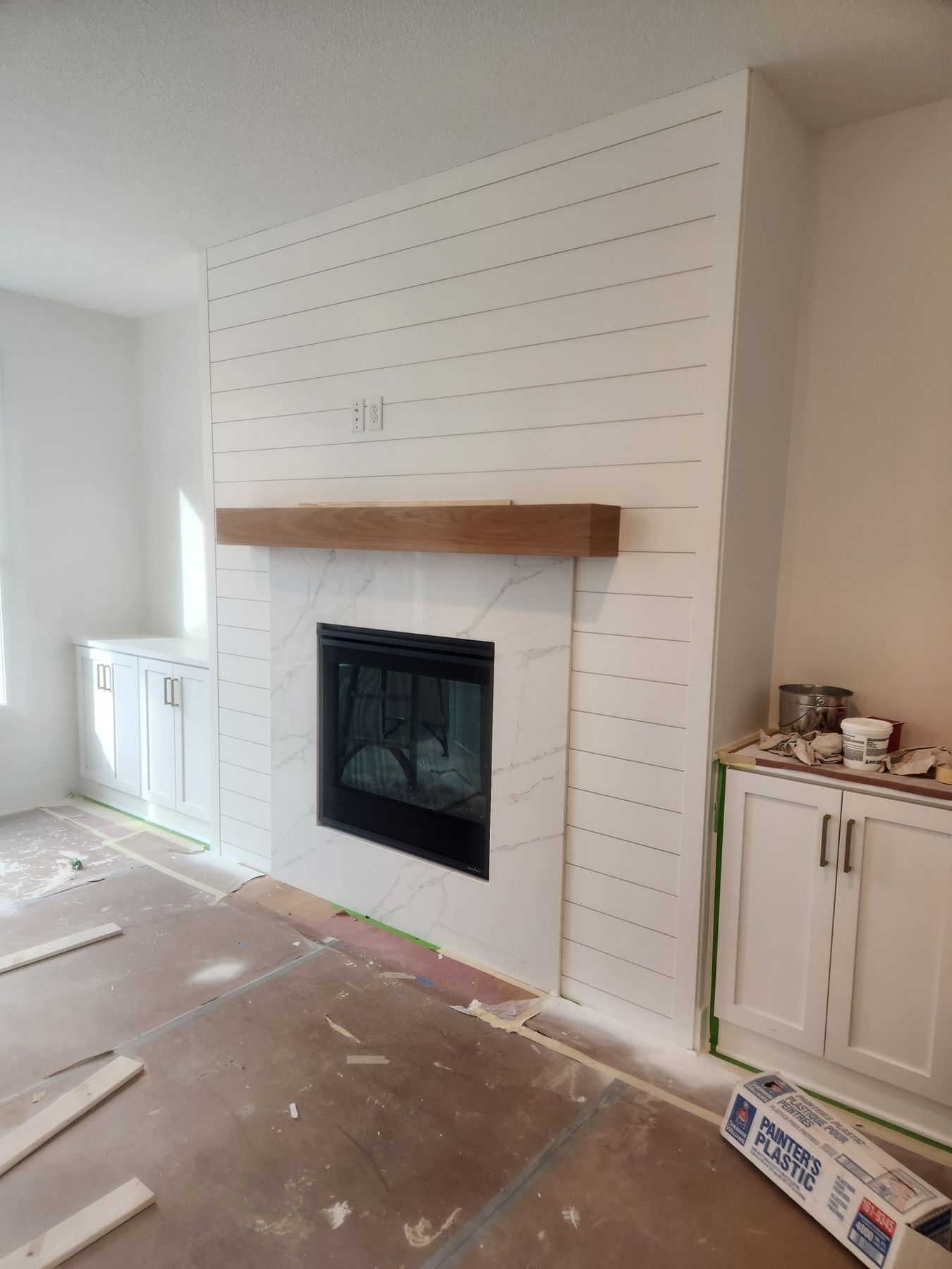 In progress: Living room with a white shiplap fireplace surround and built-ins